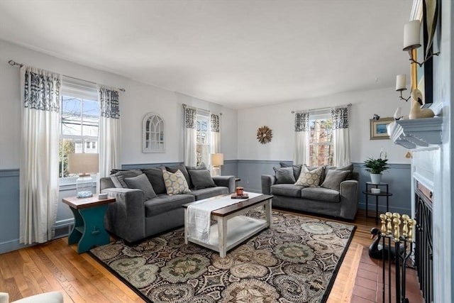 living area featuring a fireplace with flush hearth, plenty of natural light, a wainscoted wall, and hardwood / wood-style floors