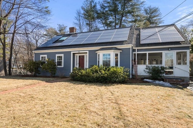 view of front of property featuring solar panels, a chimney, a front lawn, and a sunroom