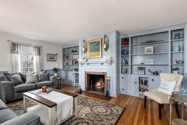 living room featuring built in shelves, a brick fireplace, and wood finished floors