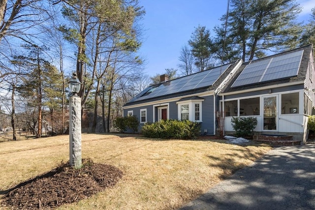 view of front of house featuring roof mounted solar panels, a chimney, a front lawn, and a sunroom