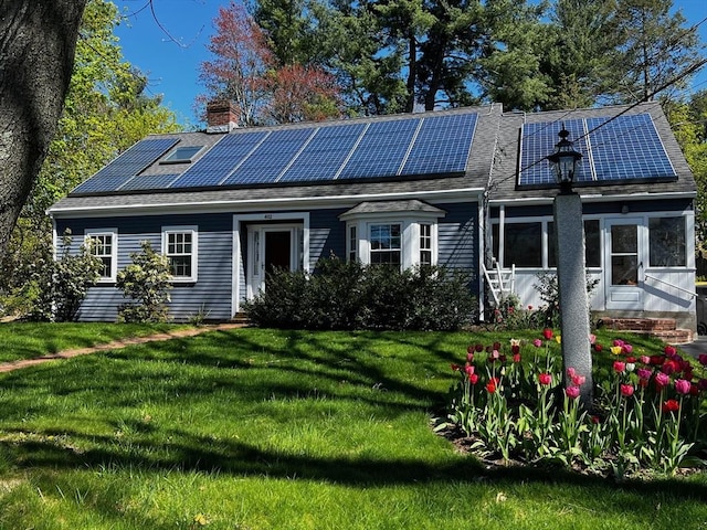 back of property with roof mounted solar panels, a lawn, and a chimney