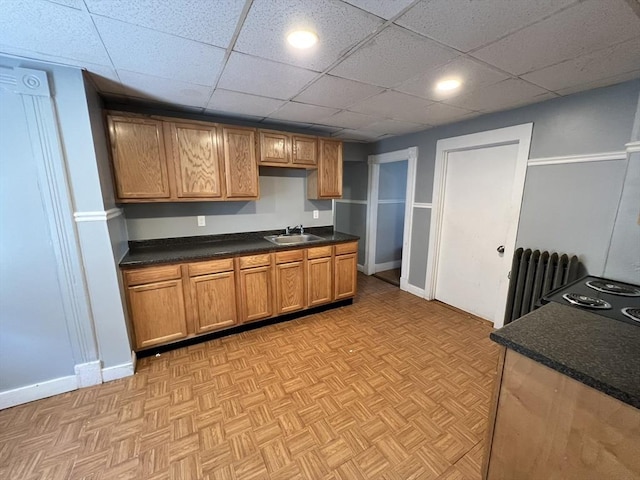 kitchen with radiator, a paneled ceiling, sink, and light parquet flooring