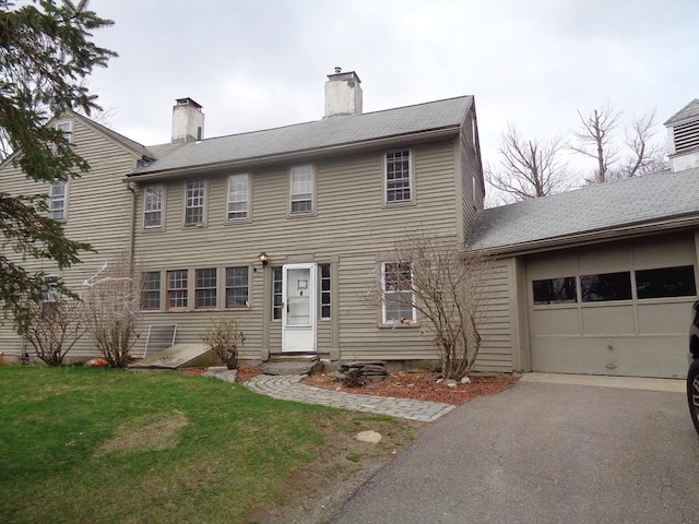 colonial inspired home with an attached garage, a chimney, a front lawn, and aphalt driveway