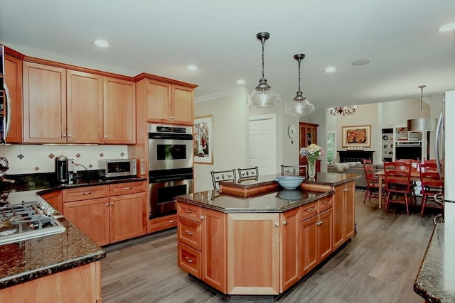kitchen with a center island, dark stone counters, light wood-style floors, pendant lighting, and appliances with stainless steel finishes
