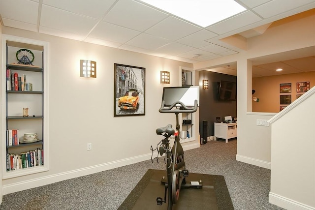 workout room featuring baseboards, carpet floors, built in shelves, and a drop ceiling