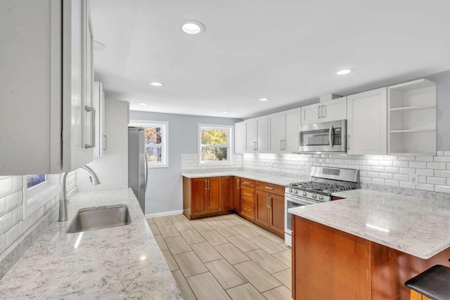 kitchen featuring a peninsula, appliances with stainless steel finishes, light stone countertops, and a sink