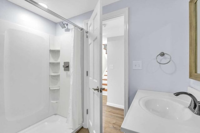 bathroom with a shower with curtain, wood finished floors, baseboards, and a sink