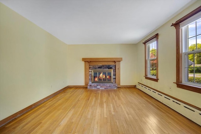 unfurnished living room featuring baseboard heating, hardwood / wood-style floors, a brick fireplace, and baseboards