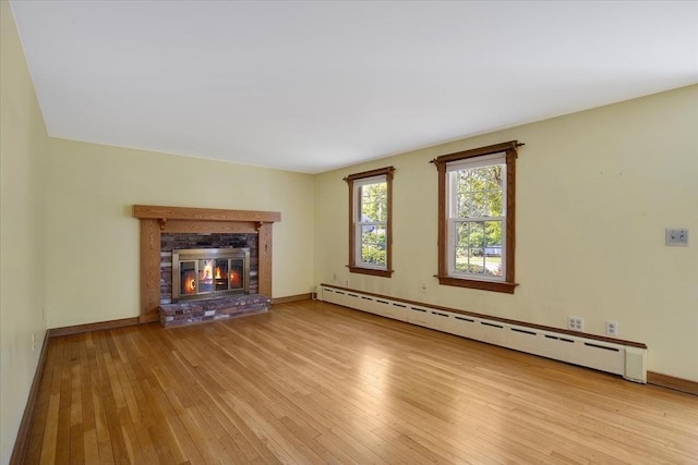 unfurnished living room featuring a baseboard heating unit, hardwood / wood-style floors, a fireplace, and baseboards