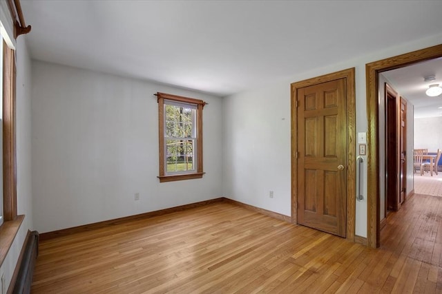 unfurnished room featuring light wood-style flooring, a baseboard heating unit, and baseboards