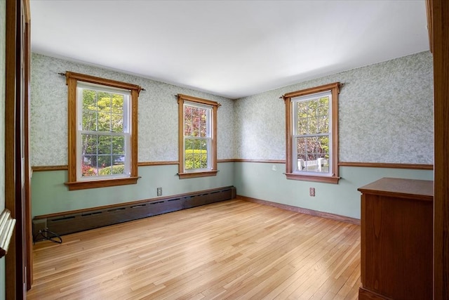 empty room with a baseboard heating unit, hardwood / wood-style floors, and wallpapered walls