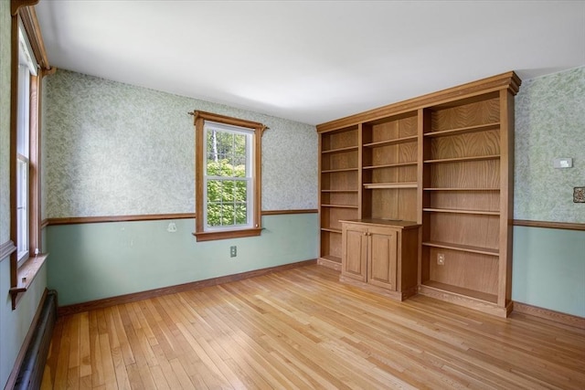 empty room with a baseboard radiator, wallpapered walls, light wood-style flooring, and baseboards