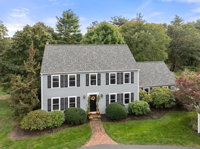 colonial house featuring a front yard and a shingled roof