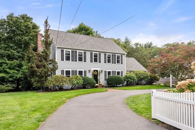 colonial inspired home with driveway, a shingled roof, a front lawn, and fence