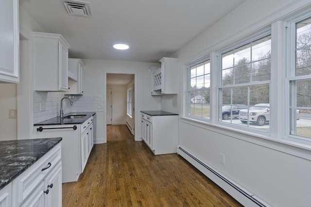 kitchen with dark wood-style floors, visible vents, a baseboard heating unit, white cabinets, and a sink