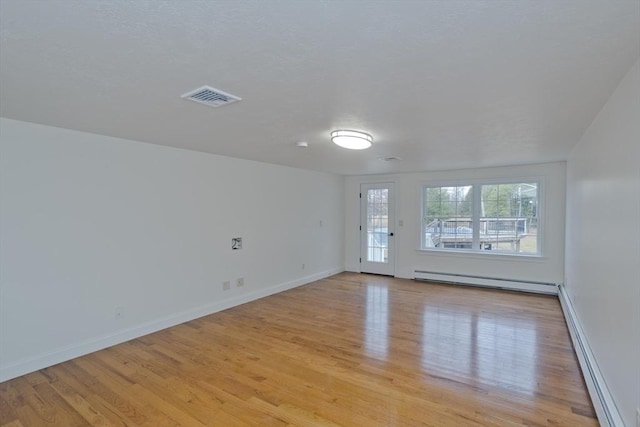 empty room featuring light wood-style floors, visible vents, and baseboard heating