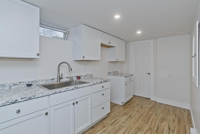 kitchen featuring light stone countertops, light wood finished floors, white cabinetry, and a sink