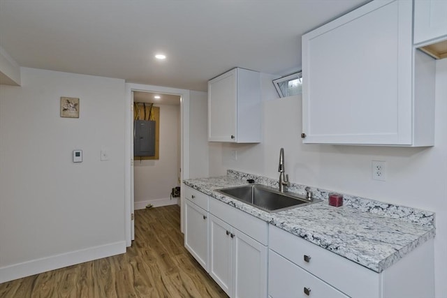 kitchen with light wood finished floors, electric panel, baseboards, white cabinets, and a sink