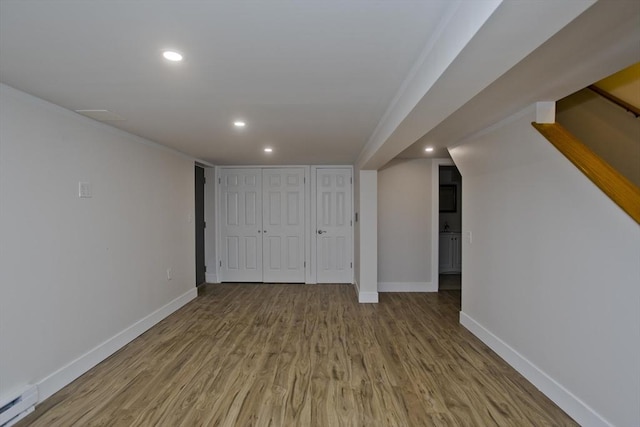 finished below grade area with recessed lighting, wood finished floors, baseboards, stairway, and baseboard heating