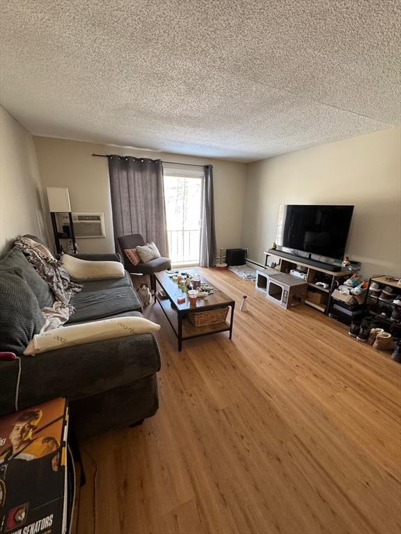 living area featuring a wall mounted AC, a textured ceiling, and wood finished floors