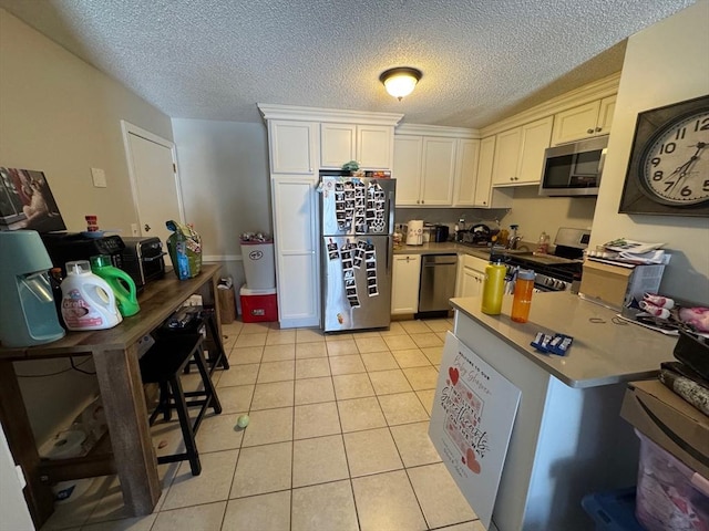 kitchen with light tile patterned floors, white cabinetry, stainless steel appliances, and a textured ceiling