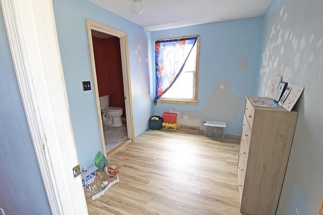 bedroom featuring light wood-type flooring, visible vents, and connected bathroom