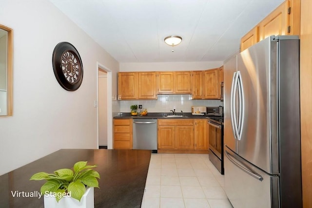 kitchen with a sink, decorative backsplash, light tile patterned floors, dark countertops, and appliances with stainless steel finishes