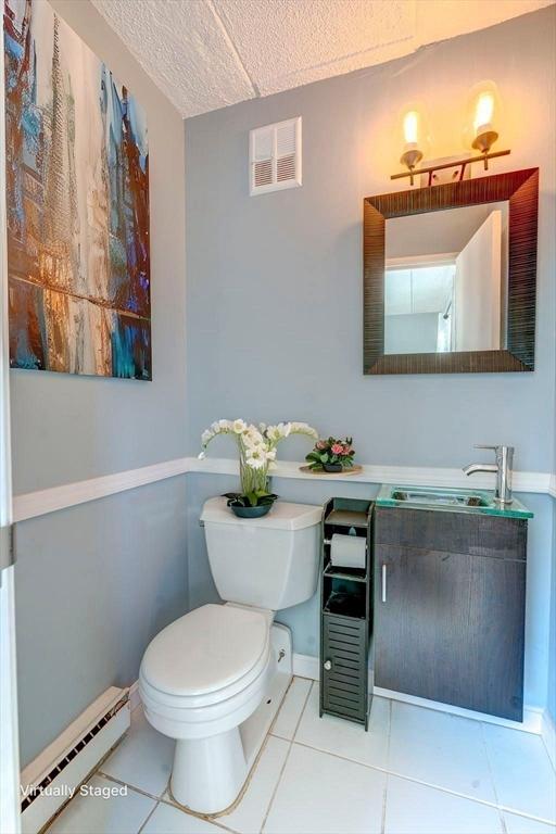 half bathroom featuring toilet, a textured ceiling, visible vents, a baseboard heating unit, and vanity