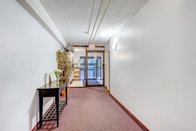 hall with a textured ceiling, baseboards, and carpet floors