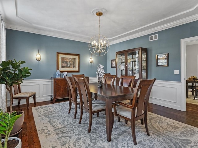 dining room featuring dark wood-type flooring, wainscoting, visible vents, and a notable chandelier