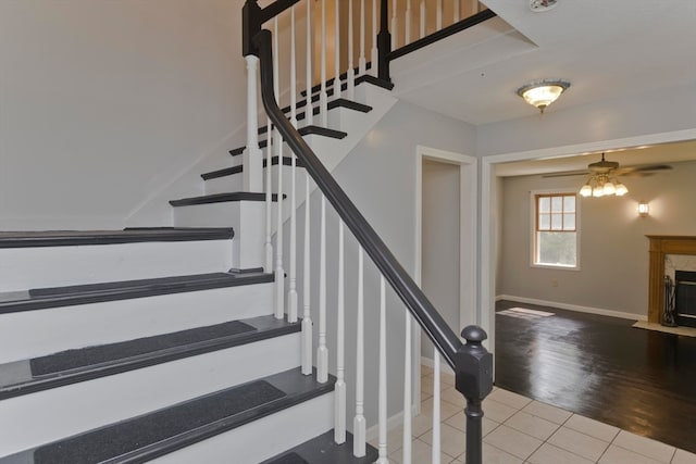 stairs featuring wood-type flooring, ceiling fan, and a fireplace