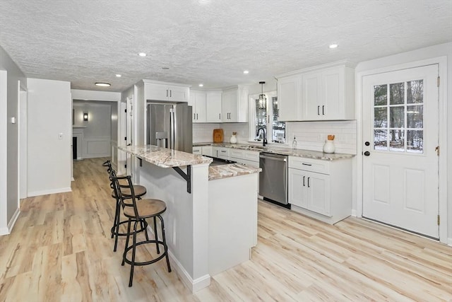 kitchen featuring appliances with stainless steel finishes, white cabinetry, a center island, light stone countertops, and decorative light fixtures