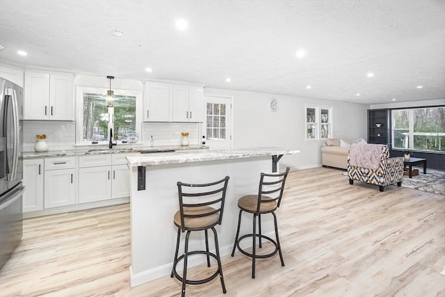 kitchen with light hardwood / wood-style flooring, white cabinetry, hanging light fixtures, a center island, and light stone countertops