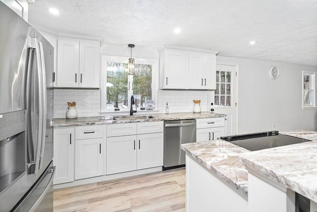 kitchen featuring appliances with stainless steel finishes, white cabinetry, hanging light fixtures, a textured ceiling, and light hardwood / wood-style flooring