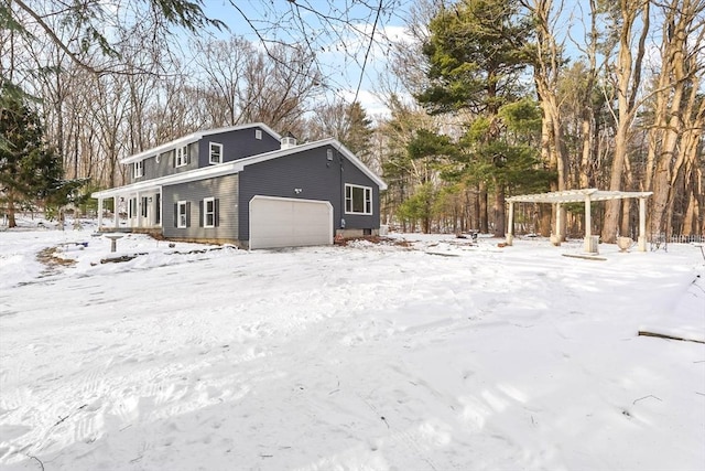 view of snowy exterior with a garage and a pergola