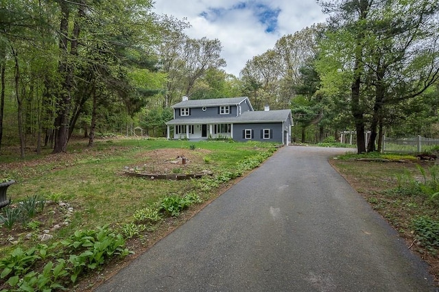 view of front facade with a chimney, a porch, driveway, and a view of trees