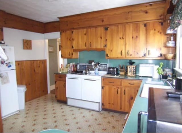 kitchen featuring white appliances, wooden walls, and sink