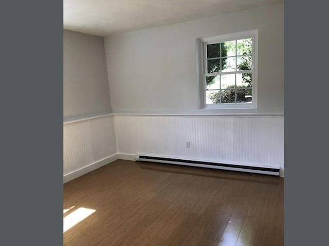 unfurnished room with baseboard heating, wainscoting, and wood finished floors
