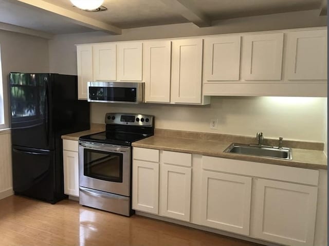 kitchen featuring white cabinets, stainless steel appliances, beamed ceiling, and a sink