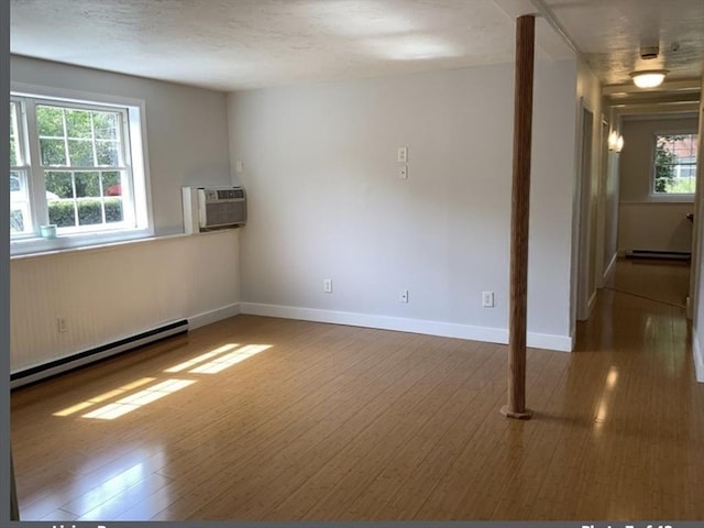 spare room featuring wood finished floors, baseboards, baseboard heating, a wall mounted AC, and a baseboard heating unit