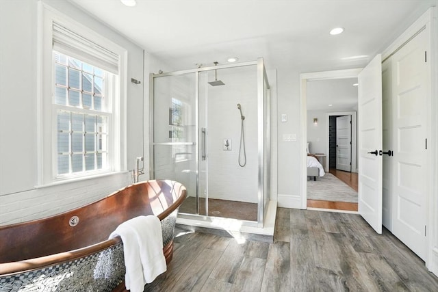 ensuite bathroom with a freestanding tub, a shower stall, recessed lighting, and wood finished floors