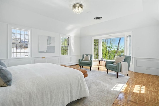 bedroom featuring visible vents, wainscoting, a decorative wall, and a notable chandelier