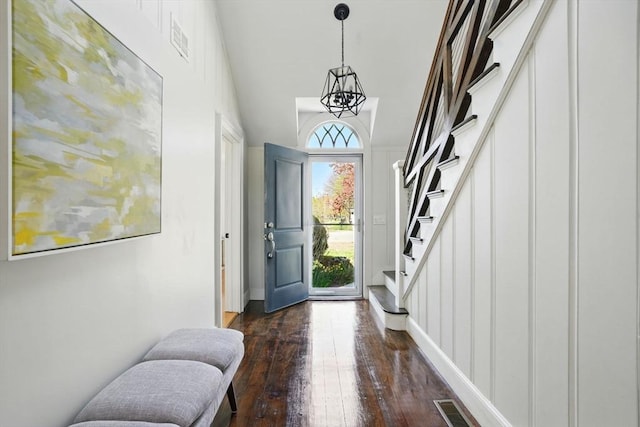 entryway featuring an inviting chandelier, stairs, baseboards, dark wood-type flooring, and visible vents