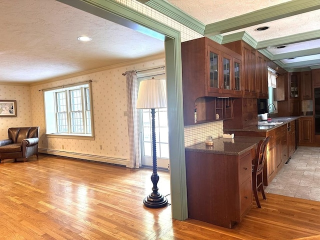 kitchen featuring crown molding, a textured ceiling, baseboard heating, light hardwood / wood-style flooring, and dark stone counters