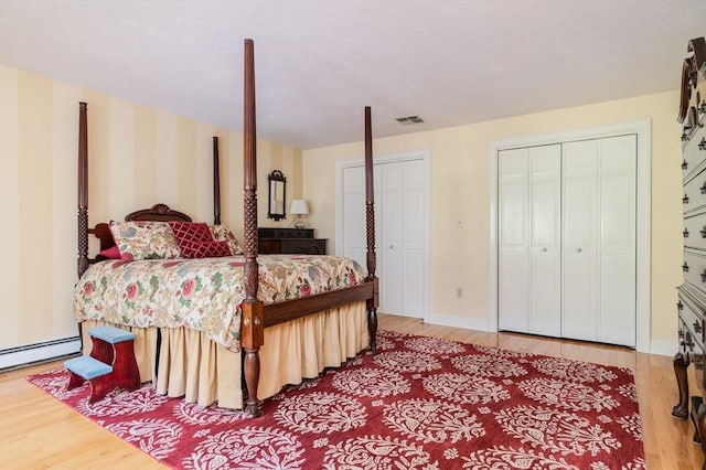 bedroom featuring two closets, a baseboard radiator, and light wood-type flooring