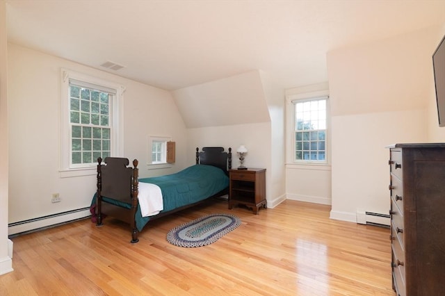 bedroom featuring light hardwood / wood-style floors, multiple windows, and a baseboard heating unit