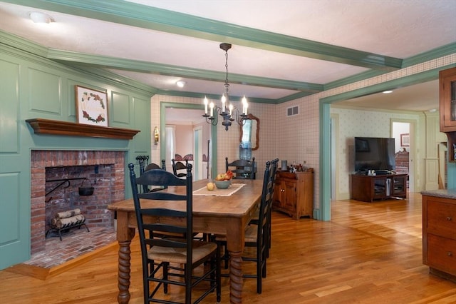 dining area featuring beamed ceiling, light hardwood / wood-style floors, ornamental molding, a notable chandelier, and a brick fireplace