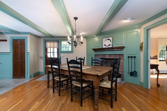 dining area with a brick fireplace, a baseboard radiator, crown molding, and light wood-type flooring