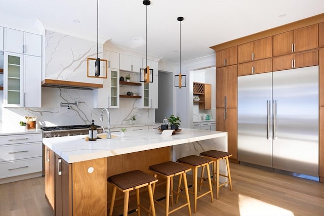 kitchen featuring built in refrigerator, light hardwood / wood-style flooring, white cabinetry, hanging light fixtures, and a center island with sink