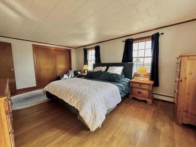 bedroom with wood finished floors, baseboards, baseboard heating, and ornamental molding